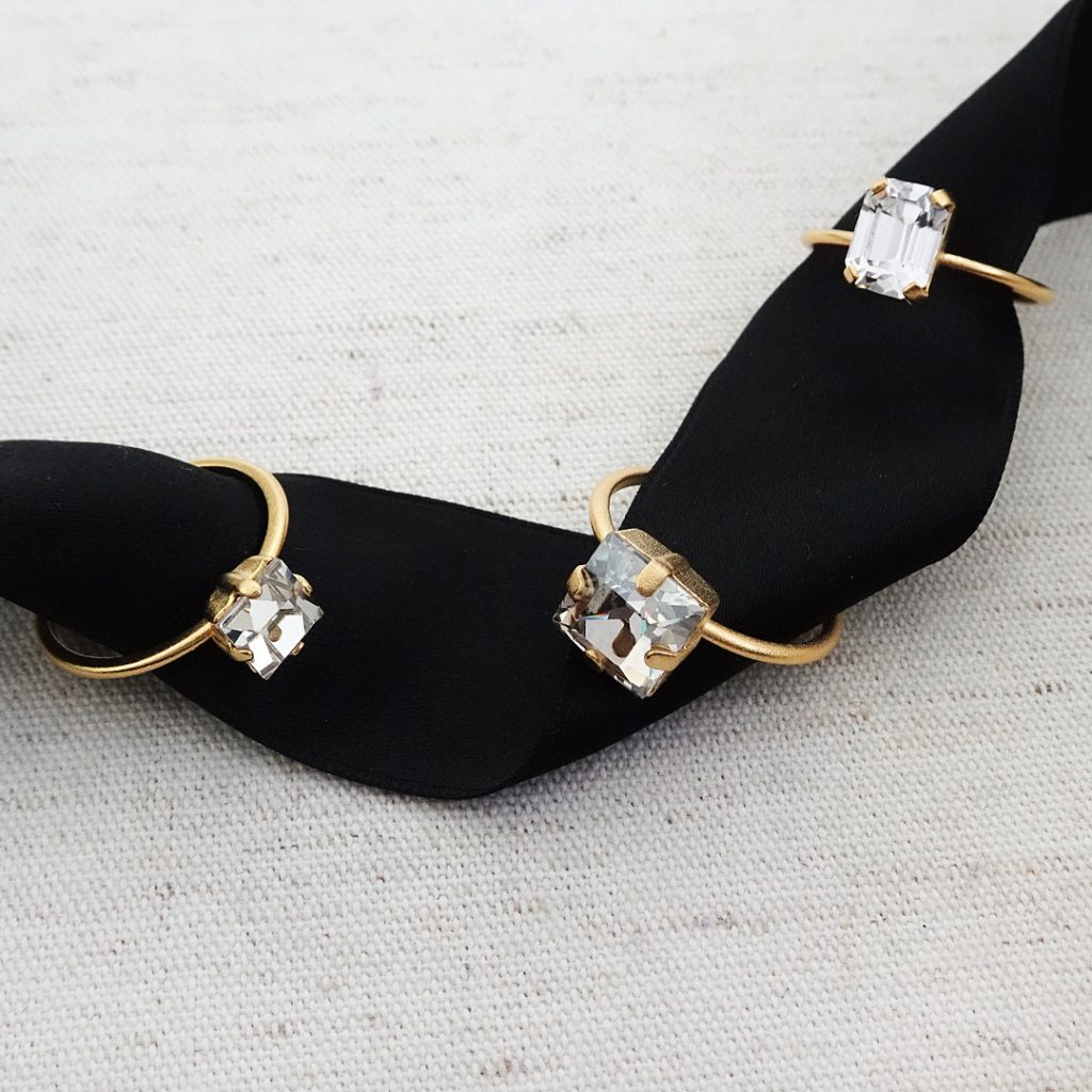 three tiny crystal rings in different shapes on thin gold bands on a black ribbon. mini rings, dainty rings